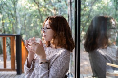 Genç kızıl saçlı kadın bir barakanın terasında çay içiyor.