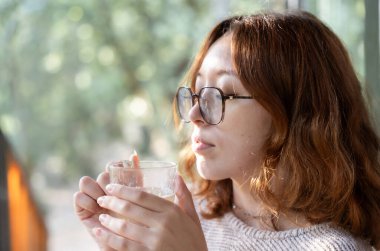 Genç kızıl saçlı kadın bir barakanın terasında çay içiyor.