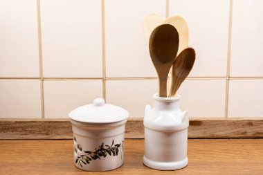 Seramik tutacakta tahta kaşıklar, mutfak tezgahında sarımsak koruyucusunun yanında.