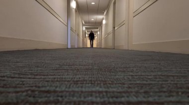 Koridorda bir adam yavaşça zemin kattaki kameraya yaklaşıyor.