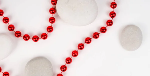 banner for web white sea stones and red beads between them on a white background. substrate, texture, red beautiful bright beads, beauty and style.