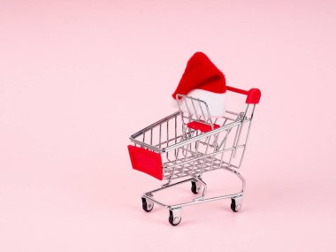 Hediye ya da hediye arabası ve karlı arka planda köknar ağacı. Noel ve yeni yıl indirimi konsepti. Noel Baba şapkası arabada..