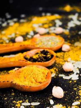 Hint ve diğer baharatlar tahta kaşıklarda, siyah bir masaya saçılmış.