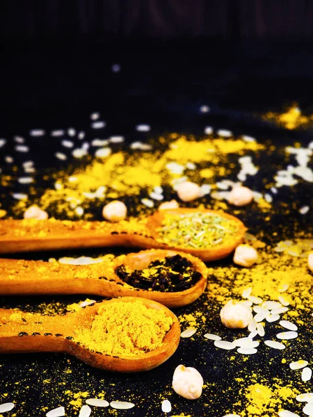 Indiska och andra kryddor i träskedar, utspridda på ett svart bord — Stockfoto