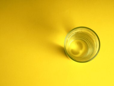 Minimalist su tüketimi kavramı, sarı arka planda bir bardak su.