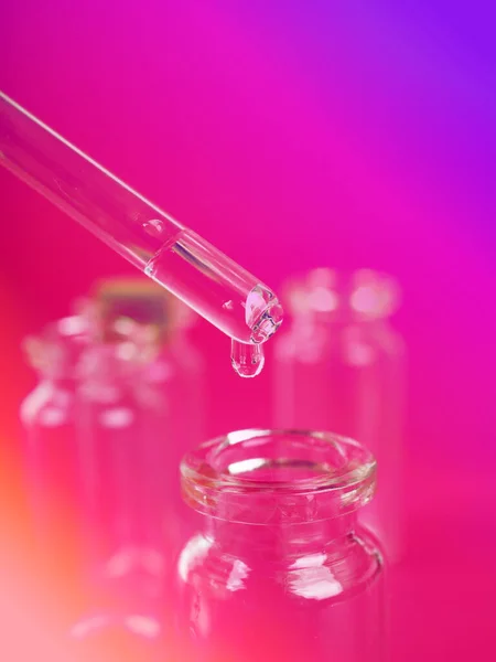 Goutte de liquide d'une pipette dans une bouteille médicale, concept de recherche, nouveaux médicaments et la science, sur un fond rose vif, bleu et violet — Photo