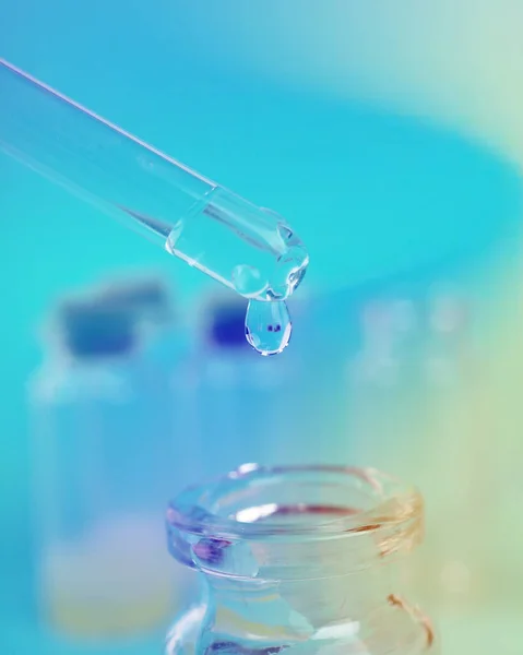 Gota de líquido de uma pipeta em uma garrafa médica, conceito de pesquisa, novas drogas e ciência, em um fundo rosa brilhante, azul e roxo — Fotografia de Stock