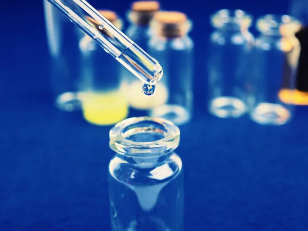 Kapka tekutiny z pipety do lékařské láhve, koncept výzkumu, nové léky a věda, na jasně růžové, modré a fialové pozadí — Stock fotografie