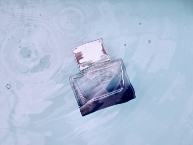 Mavi şeffaf parfüm şişesi, suyun altında, üzerinde dalgalar.