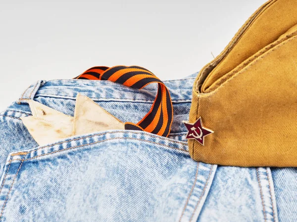 Modern jeans and symbols of victory in the Second World War. St. Georges ribbon, military cap, cartridges and letters from the front. The concept of victory on May 9 for a postcard background