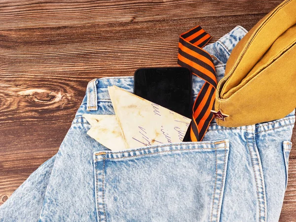 Modern jeans and symbols of victory in the Second World War. St. Georges ribbon, military cap, cartridges and letters from the front. The concept of victory on May 9 for a postcard background