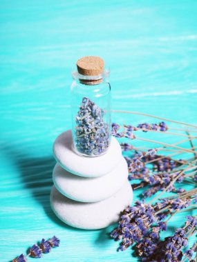 Mavi ahşap arka planda Zen taşları şişede lavanta tohumları ve yakınlarda lavanta dalları..