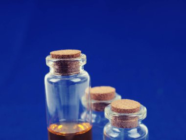 Birkaç tıbbi şişe, mavi arka planda tıpası olan test tüpleri..