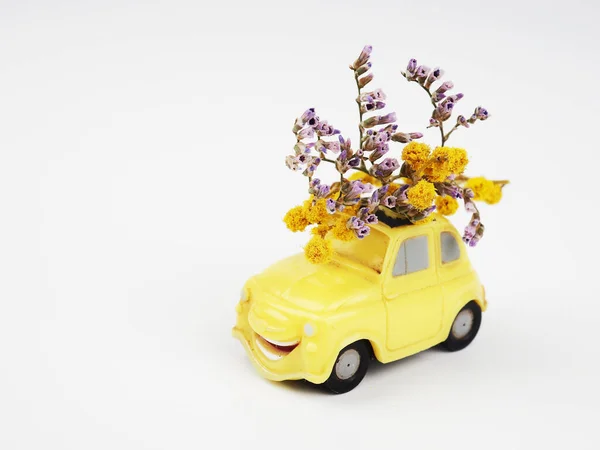 Small yellow toy car with a bouquet of wild flowers on a white background.