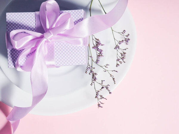 A gift box with a lilac ribbon lies on the plates saucers.