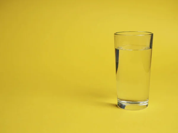 minimalistic concept of water consumption, one glass of water on a yellow background.