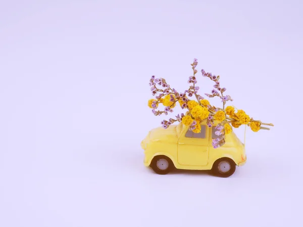 Small yellow toy car with a bouquet of wild flowers on a white background.