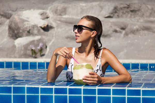 Une femme dans une piscine de maillot de bain lumineux avec noix de coco — Photo