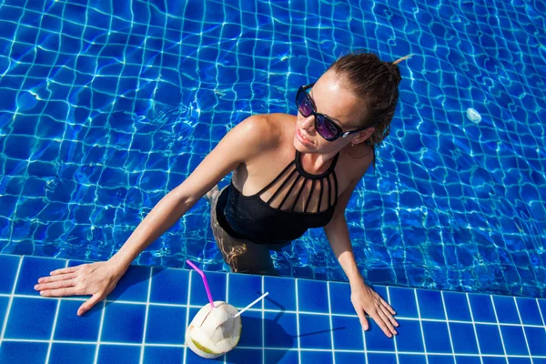 Die Frau im schwarzen Badeanzug im blauen Pool mit Kokosnuss — Stockfoto