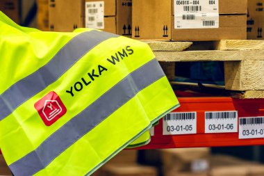 MOSKOW, Rusya - 16 ARALIK 2020 YOLKA WMS rozet Sarı sinyal yelek yakın görüş. Yolka Depo yönetim sistemi. Depo binasında bir paletin ve kutuların üzerinde duran işaret yeleği..