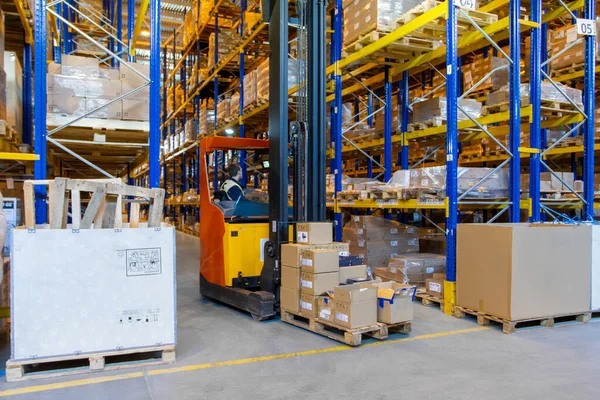Depo işçisi depodaki yüksek mavi çelik raflar arasında forklift dolu bir kamyon kullanıyor.