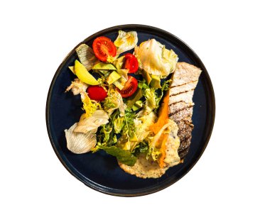 Taze yeşil salatalı ızgara balık filetosu, beyaz arka planda izole edilmiş koyu bir tabakta kiraz domatesleri ve kremalı sos. Kopya alanı ile sağlıklı gurme yemek kavramı.