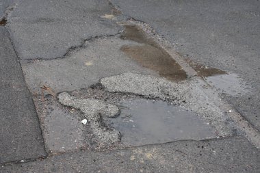 Caddenin ortasında çatlaklar olan eski asfalt yol.