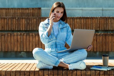 İş kadını halka açık bir parkta bankta oturuyor, dizüstü bilgisayarda çalışıyor. Kot giymiş çekici esmer kız. 