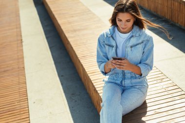 Kız öğrenci halka açık bir parkta oturuyor ve cep telefonu kullanıyor. Güzel esmer kadın arkadaşlarıyla mesajlaşıyor.