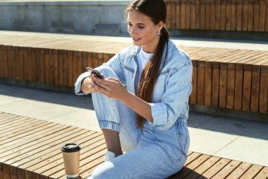 Öğrenci halka açık parkta oturuyor ve cep telefonu kullanıyor. Güzel esmer kadın arkadaşlarıyla mesajlaşıyor.