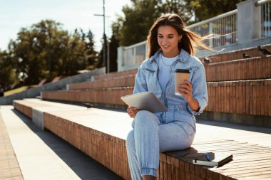 Milenyum kotlu kızı elinde akıllı bir tabletle parktaki bankta oturuyor. Kadın tablet kullanıyor