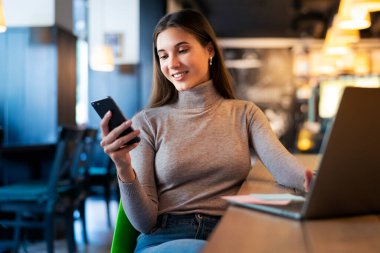 Çekici iş kadını dizüstü bilgisayarın önünde oturuyor ve cep telefonuyla konuşuyor, telefonda görüşüyor.. 