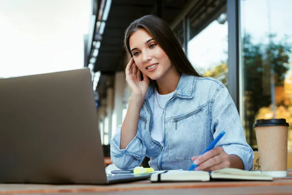 Joven mujer de negocios que trabaja en la terraza abierta en casa, sentada frente a la computadora portátil, sosteniendo el teléfono inteligente en su mano. — Foto de Stock