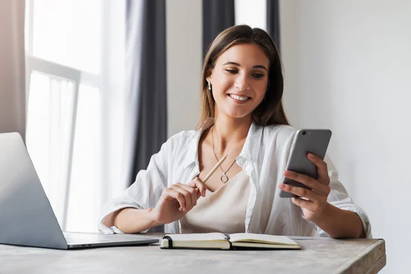 Attractive business woman sits at table in front of laptop and talks on mobile phone, negotiates on the phone.