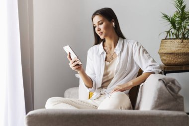 Kadın evde dinleniyor, akıllı telefonu mesajlarda kullanıyor, fotoğrafları paylaşıyor, arkadaşlarla iletişim kuruyor, e-postaları kontrol ediyor