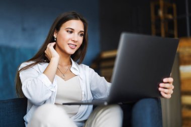 Çekici iş kadını dizüstü bilgisayarın önünde bir koltuğa oturur, çevrimiçi bir konferans aracılığıyla konuşur, pazarlık eder.