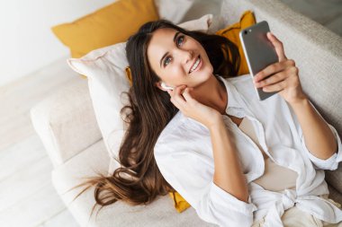 Beyaz gömlekli gülümseyen esmer, koltukta rahat bir şekilde uzanıyor ve akıllı telefondan konuşuyor. Kadınlar arkadaşlarıyla iletişim kurar.