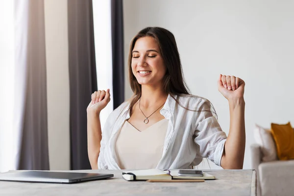 Beautiful brunette woman has completed business project, is happy. Girl sits at desk in home office. Distance work — Stock Photo, Image