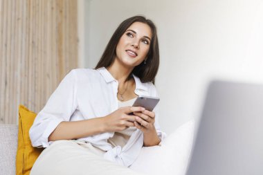 Kadın evde dinleniyor, akıllı telefonu mesaj atmak için kullanıyor. Çekici esmerin yakın plan portresi..