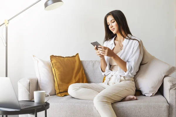 Female relaxing at home, using smartphone to text messages, share photos, communicate with friends, check email — Stock Photo, Image