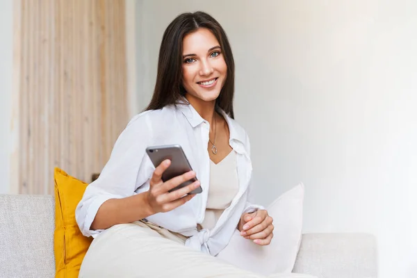 Donna che si rilassa a casa, utilizzando lo smartphone per i messaggi di testo. Ritratto ravvicinato di bruna attraente. — Foto Stock