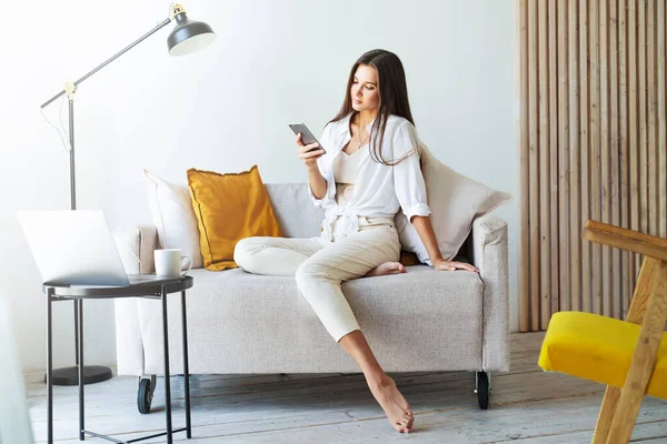 Kobieta relaksująca się w domu, korzystająca ze smartfona do pisania SMS-ów, udostępniania zdjęć, komunikowania się ze znajomymi, sprawdzania poczty e-mail — Zdjęcie stockowe