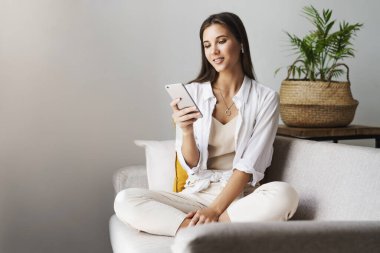 Kadın evde dinleniyor, akıllı telefonu mesajlarda kullanıyor, fotoğrafları paylaşıyor, arkadaşlarla iletişim kuruyor, e-postaları kontrol ediyor