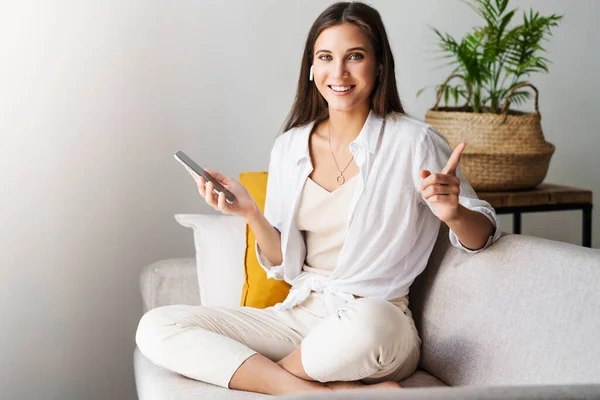 Female relaxing at home, using smartphone to text messages, check email, looking at the camera with showing success.. — Stock Photo, Image