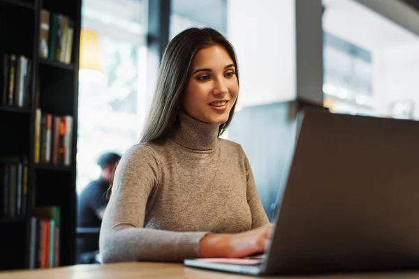 Atractiva mujer de negocios se sienta en la mesa delante de la computadora portátil, funciona de forma remota, mientras que en la cafetería. — Foto de Stock