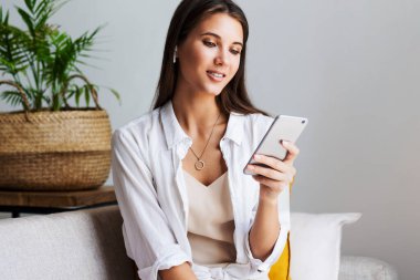 Kadın evde dinleniyor, akıllı telefonu mesajlarda kullanıyor, fotoğrafları paylaşıyor, arkadaşlarıyla iletişim kuruyor.