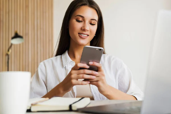 Çekici iş kadını dizüstü bilgisayarın önünde oturuyor ve cep telefonuyla konuşuyor, telefonda görüşüyor.. 