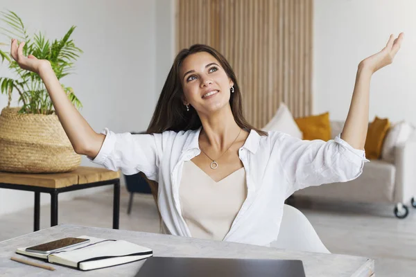 Girl sits at desk in home office and shows joyful gesture with her hands. — Stock Photo, Image