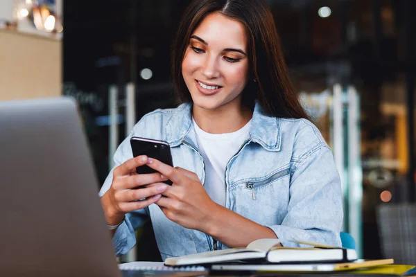 Attraktive forretningskvinne sitter ved bordet foran laptop 'en og snakker i mobiltelefon, forhandler på telefon. – stockfoto