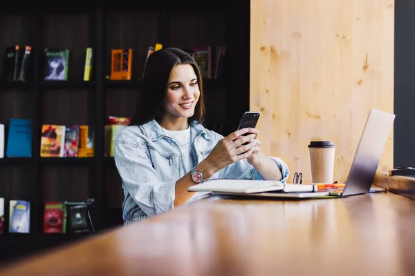 Attraktive forretningskvinne sitter ved bordet foran laptop 'en og snakker i mobiltelefon, forhandler på telefon. – stockfoto